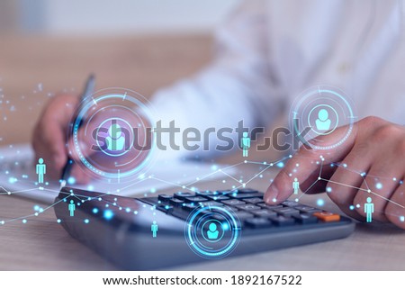 HR specialist researching and analyzing the data of salary on employment market to forecast ongoing expenses of the company using calculator. Hiring new talented officers. Social media hologram icons Royalty-Free Stock Photo #1892167522