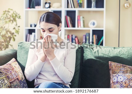 Young woman sitting on sofa covered  freezing blowing running nose got fever caught cold sneezing in tissue, sick girl having influenza symptoms coughing at home, flu concept Royalty-Free Stock Photo #1892176687
