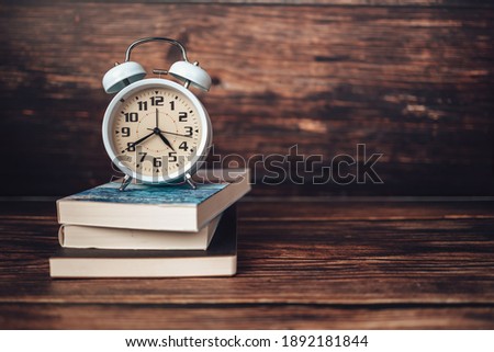 Alarm clock on book stack on wood table.