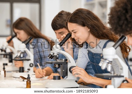 Group of college students performing experiment using microscope in science lab. University focused student looking through microscope in biology class. High school girl examine samples during lecture Royalty-Free Stock Photo #1892185093