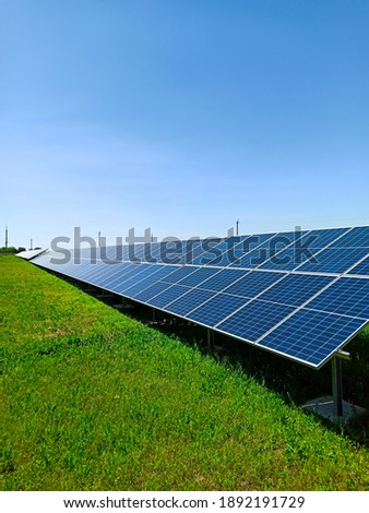A row of solar panels stand on green field, against the blue sky. A symbol of clean energy, concern for the environment, a concept.