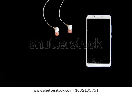  broken phone with headphones on black background                      