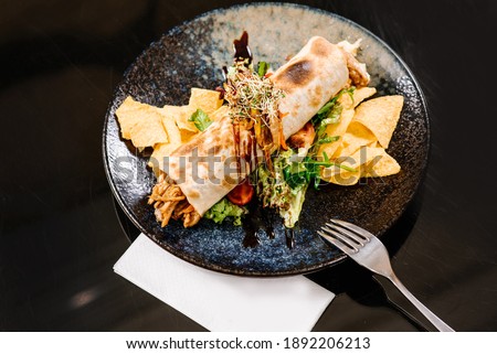Roll filled with pulled pork meat with green salad and chips on dark background