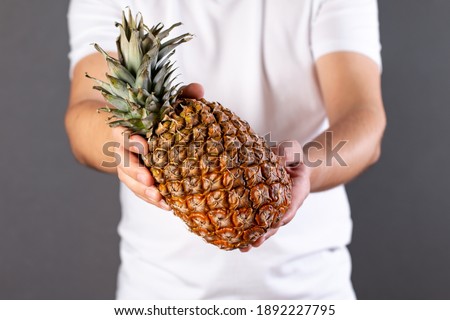 Young man holding a ripe and juicy pineapple. Appropriate healthy nutrition, vitamin concept, soft focus