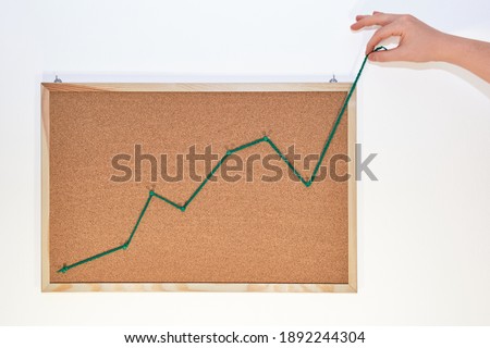 Savings, investment and off the charts concept. Hand pulling the line of a growing graph outside the cork board. Royalty-Free Stock Photo #1892244304