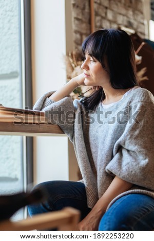 Beautiful woman with hand on chin looking away in cafeteria. Picture of young pretty woman sitting at the table in cafe and reading book.