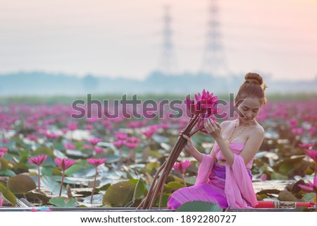 Thai woman wearing traditional dress harvest lotus flower in garden