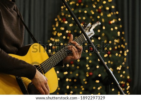 Young man playing guitar.Festive atmosphere around - bright bokeh on the background.Close up photography.