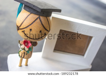 Wooden doll wearing a hat and holding flowers and white picture frame.
