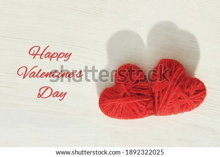 Two red hearts handmade from wool threads on a wooden light background. Card with text Happy Valentin's day.