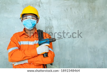 Portrait of man construction worker wearing protective mask with power drill and safety hard hat at construction site,Engineer,Construction concept,Coronavirus has turned into a global emergency.