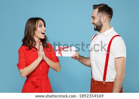 Excited cheerful happy young couple two friends man woman wearing white red clothes hold gift certificate isolated on pastel blue color background studio portrait. St. Valentine's Day holiday concept