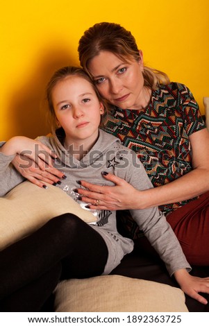 girl with mom at home on black sofa at yellow wall