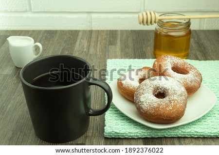 Freshly baked donuts with powdered sugar and honey with coffee. Powdered donuts and coffee with honey with space for text.