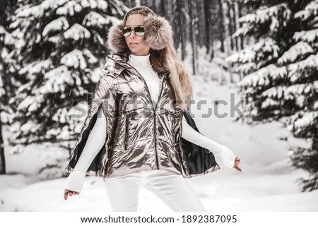 Young woman winter portrait. Winter fashion model with white winter outfit and sunglasses. Attractive young woman in wintertime outdoor. Mountains, white snow in magic winter day.
