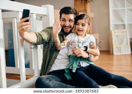 Happy little girl and her father having fun while taking selfie after moving into new home. 