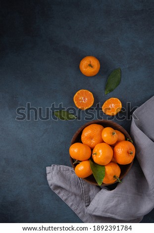 sweet tangerines with green leaves in wooden bowl  on a dark blue background with gray napkin. Dark photo. Top view and copy space