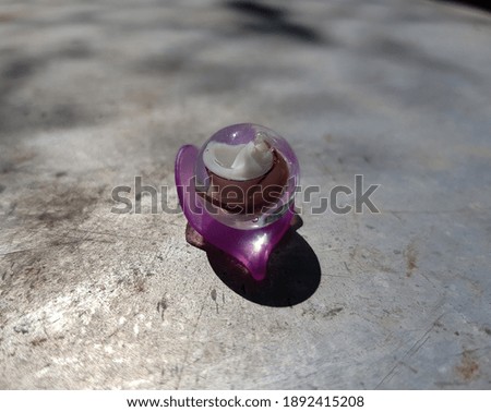 A round glass bead with a spiral decor inside - on a purple plastic petal, in the sun, on an old gray tin (side view).