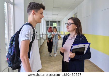 School, college, female teacher talking to a male teenage student in school corridor. Adolescence and education Royalty-Free Stock Photo #1892432797