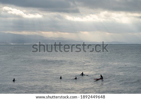 Five silhouettes of friends on their surf in the Atlantic ocean water. Sunset in the Plage des Basques beach. Mountains in background. Winter sun light with clouds in Biarritz, France, Europe.