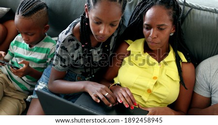 African american family looking at computer laptop at home sofa. Mother and teen daughter browsing internet together.