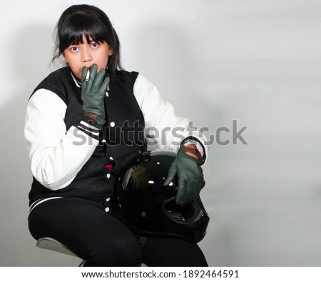 Young mother motorcyclist smokes while wearing a jacket, helmet and leather gloves