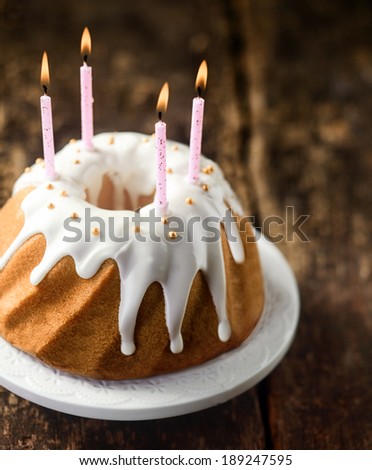 Party candles burning on a twirled vanilla ring cake decorated with icing and pearls to celebrate a happy birthday , high angle view on a rustic wooden background
