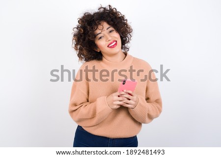 Young beautiful Arab woman wearing knitted sweater standing against white background Mock up copy space. Using mobile phone, typing sms message