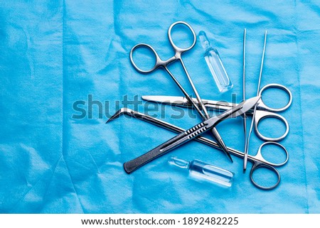 stack of surgical equipment at surgery desk. medical tools such scissors, scalpel, forceps, tweezers over blue background. surgery concept. Royalty-Free Stock Photo #1892482225