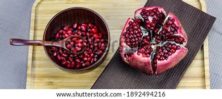 Wooden bowl containing wooden spoon and red pomegranate seeds. Pomegranate fruit open divided into five parts held together on a napkin  cloth on wooden tray on a blue background. Fruit pomegranate.