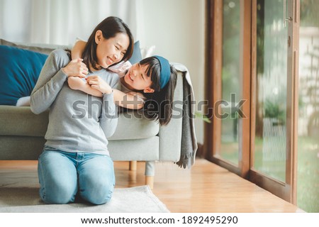Happy Asian mother and cute little daughter having fun while playing and hugging at home in living room