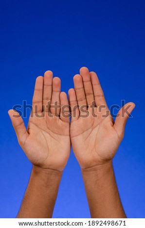 Empty hands showing palms, thanking, raised to the sky, on blue background.