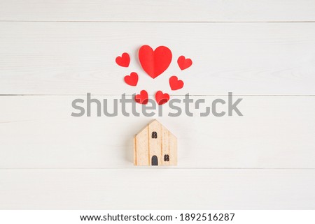 Wood house with heart shape paper on white wooden desk background, love and harmony of family, residence and insurance, symbol and sign, top view, flat lay, copyspace, nobody.