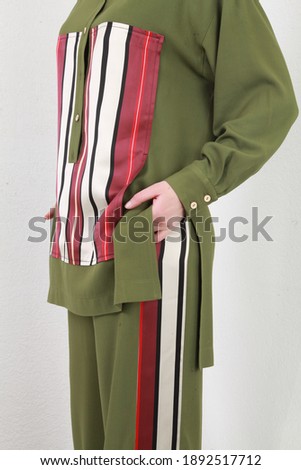 Front side cropped shot of unrecognizable model in trendy clothes, wearing green spring summer suit with stripes and posing over white walls background. High key image. Fashion close up details
