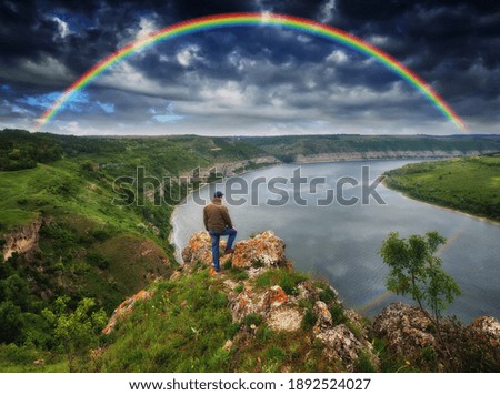 colorful rainbow over the river. man on a rock above the canyon