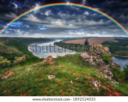 colorful rainbow over the river. man on a rock above the canyon