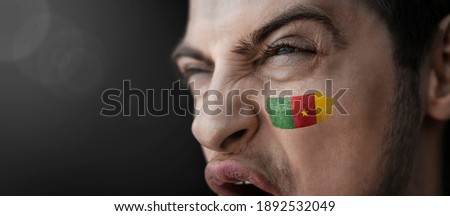 A screaming man with the image of the Cameroon national flag on his face.