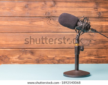 Stand with a modern microphone on a blue table on a wooden background. Sound recording equipment.