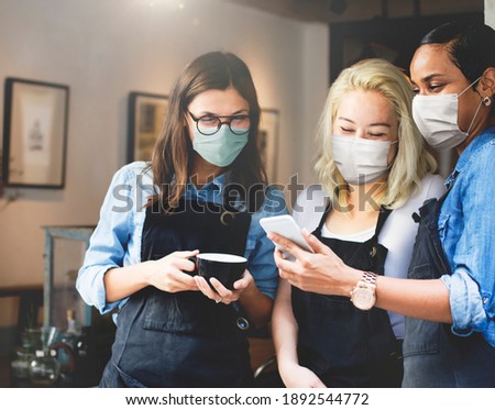 Happy baristas wearing masks looking at a phone in a cafe