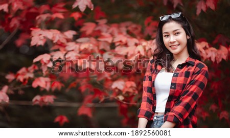 Banner Happy Portrait of a beautiful young woman with autumn leaves, Looking at the camera with a smile on a background of blurry fall trees, Holidays concept 