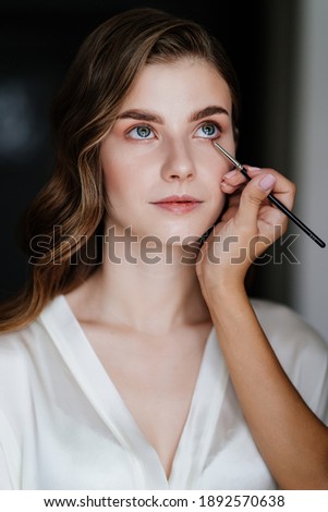 A beautiful young woman with long hair doing makeup for a wedding or photo shoot. the work of a make-up artist. the morning of the bride. decorative cosmetics.