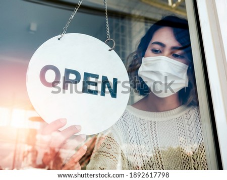 Open sign hanging on the glass door, soft focus. Woman hand flip OPEN, round sign for reopening of a small business activity after the covid-19 or Coronavirus pandemic.