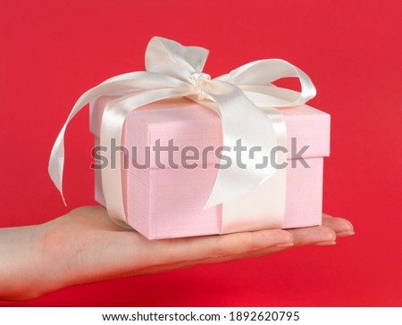 Woman's hand holding a gift with a white bow on a red background. 