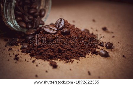 Coffee beans in a pile of ground coffee powder poured on a wooden table.