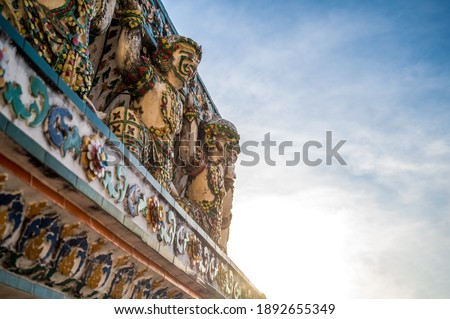 Closeup decorative Thai art stucco of giants and monkeys lifting up the pagoda base at Wat Arun Ratchawararam (Temple of Dawn) at sunset, Bangkok, Thailand