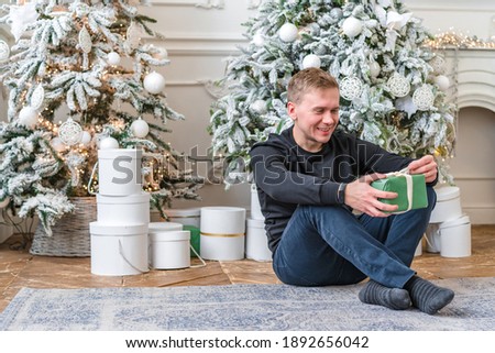 Happy man with New Year's gifts sitting on carpet on Christmas background. Cheerful white male model at Christmas in the studio.