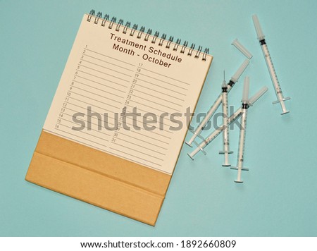 October treatment schedule calendar and disposable injection syringe on blue background