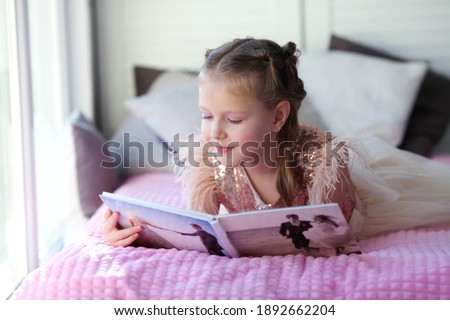 A little beautiful girl lies on the bed and looks at her parent is wedding photo album. Photo printing.