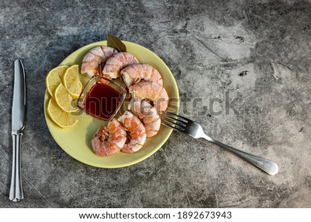 On a green platter, king prawns with lingonberry sauce, lemon and cutlery on a concrete background. Healthy eating concept