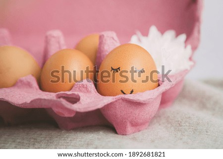 chicken egg with painted face and smile in pink egg box